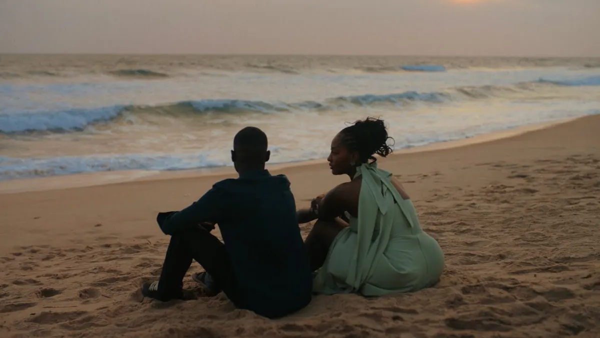 Two people sitting on a beach at dusk looking out to sea, a frame from the Raindance music video.